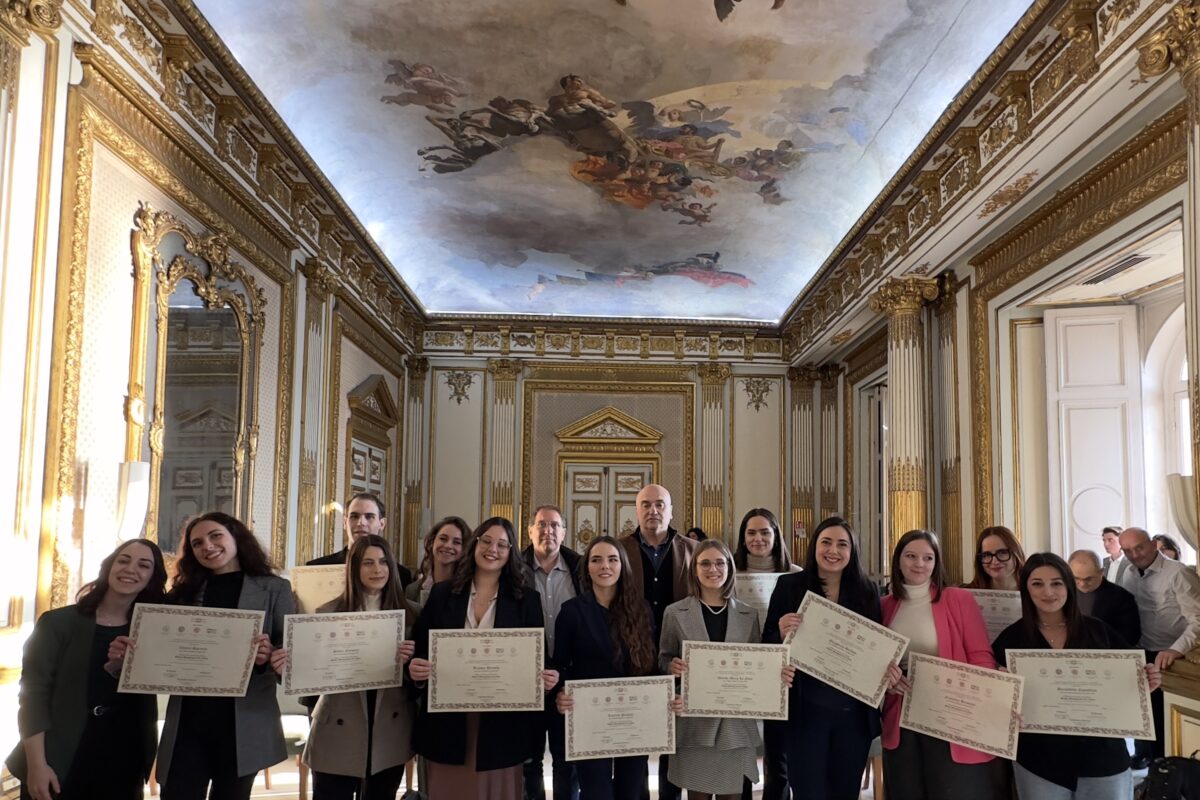 Foto di gruppo della cerimonia conclusiva del Master GMC 2024, con i partecipanti che mostrano i loro diplomi in una sala ornata da decorazioni dorate e affreschi sul soffitto.